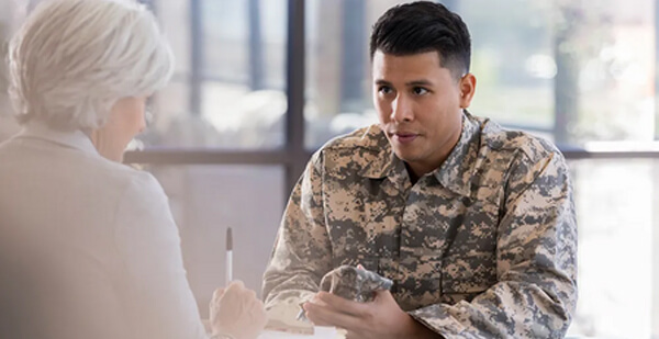 Young army soldier listens as a female therapist gives him advice regarding low blood sugar. The therapist is taking notes in the patient's chart.
